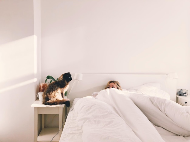 Gatto seduto accanto alla donna nel letto