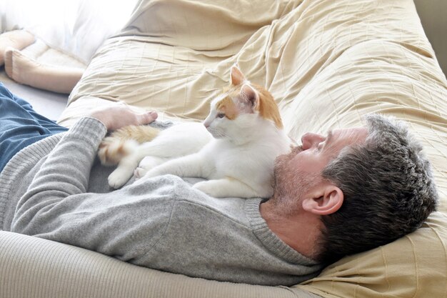 Gatto seduto sul petto di un uomo su un divano