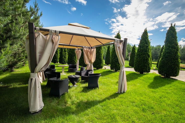 Gazebo in tela bianca con mobili da giardino in plastica in un prato verde estivo.