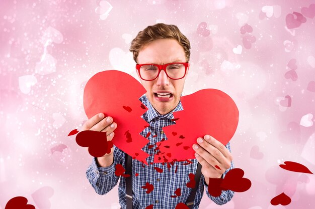 Geeky hipster che tiene un cuore spezzato contro il design del cuore di San Valentino