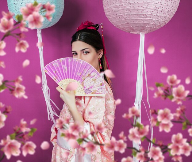 Geisha in kimono rosa e con un primo piano a ventaglio su una parete viola e con fiori sakura sfocati