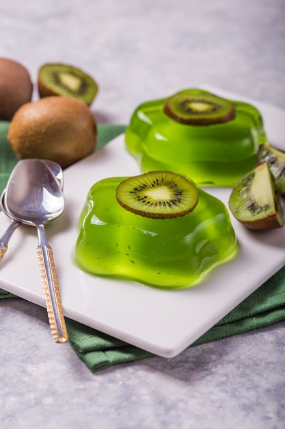 Gelatina verde fresca deliziosa due con le fette del kiwi sulla tavola concreta