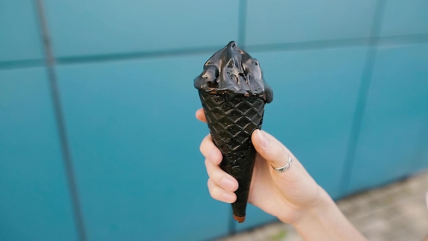 Gelato al carbone nero in una mano femminile su sfondo blu