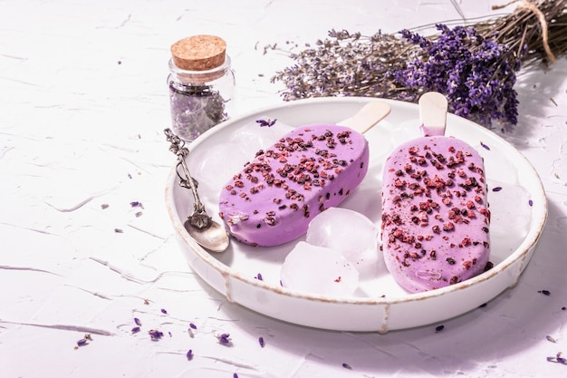 Gelato al gusto di lavanda viola. Bouquet di fiori, cucchiaio d'argento vintage, supporto in ceramica. Luce dura moderna, ombra scura. Sfondo bianco stucco, copia spazio