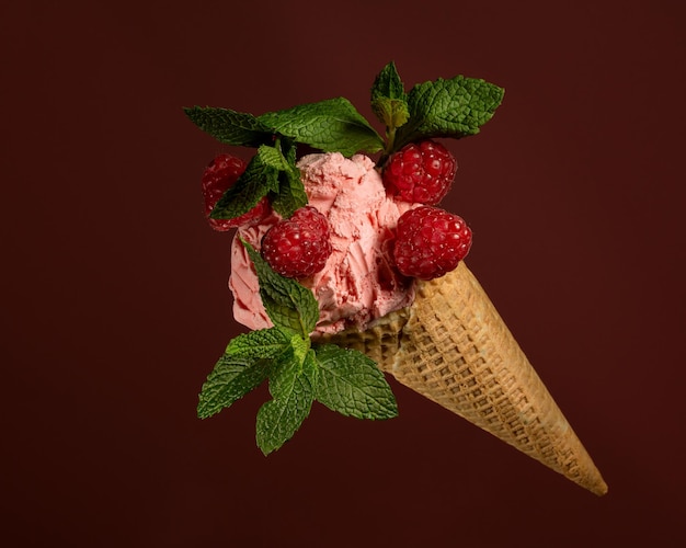 gelato al lampone con lamponi e foglie di menta, in un cono di cialda su fondo bordeaux