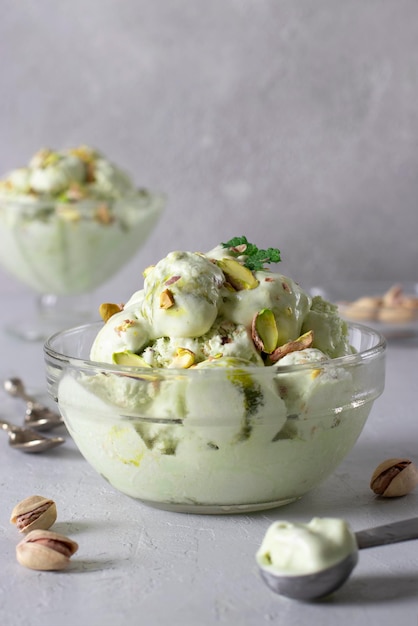 Gelato al pistacchio con noci in una ciotola di gelato di vetro trasparente su sfondo grigio chiaro