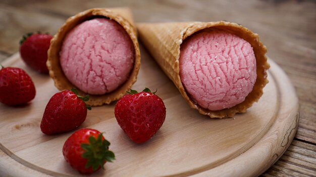 Gelato alla fragola in un cono di cialda. Bacche rosse e palline di gelato su uno sfondo di legno.