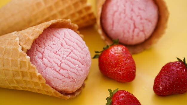 Gelato alla fragola in un cono di cialda. Gelato e frutti di bosco su sfondo giallo estivo