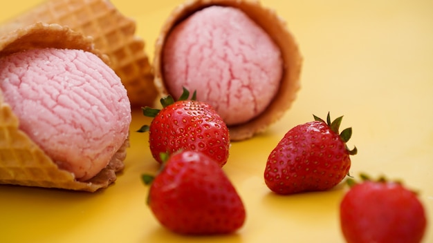 Gelato alla fragola in un cono di cialda. Gelato e frutti di bosco su sfondo giallo estivo