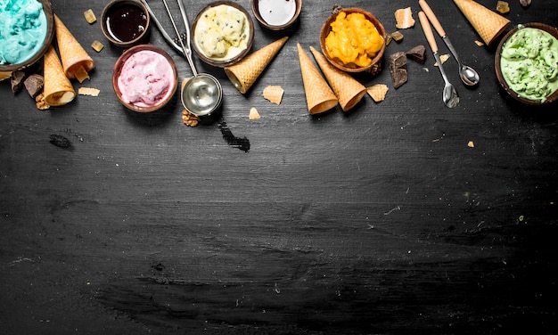 Gelato alla frutta diversa in ciotole con coppe di cialda sulla lavagna nera