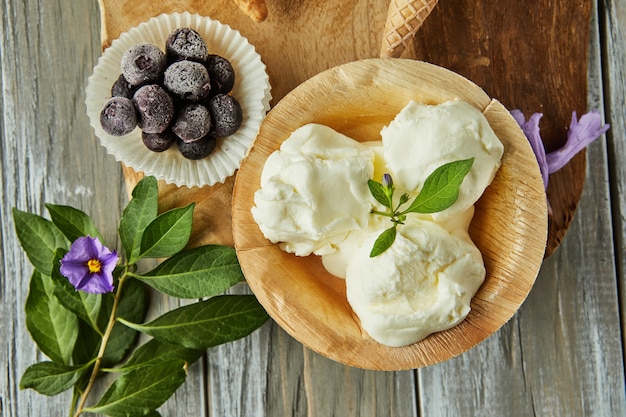 Gelato alla vaniglia in tazza su tavola di legno con frutti di bosco e fiori.