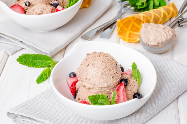 Gelato artigianale al cioccolato cremoso in una ciotola con frutti di bosco e menta. Semifreddo al gelato al cioccolato.