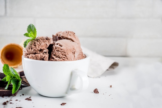 Gelato artigianale al cioccolato servito con coni di menta fresca, cioccolato fondente e waffle, spazio copia marmo bianco sfondo