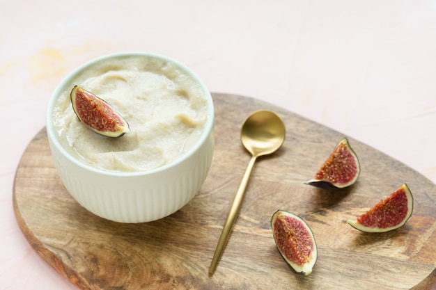 Gelato artigianale senza glutine di banana e mango giallo vegano fatto in casa con fichi freschi in una ciotola di porcellana con un cucchiaio d'oro, sfondo rosa. Copia spazio, messa a fuoco selettiva.