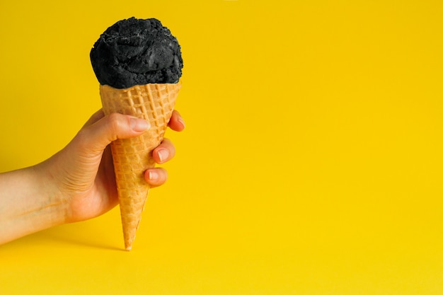 Gelato del cono della cialda della tenuta della mano femminile con carbone nero