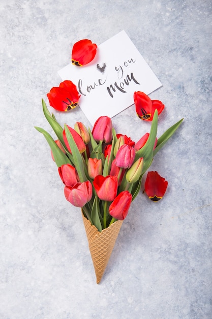 Gelato di fiori di tulipano rosso in cono di cialda con carta Ti amo mamma sulla vista concreta del piano d'appoggio nello stile piano di disposizione.