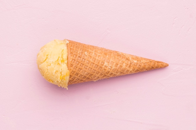 Gelato giallo della frutta nel cono della cialda su fondo rosa