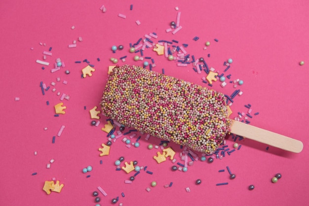 Gelato su stecco con confettini colorati su sfondo rosa