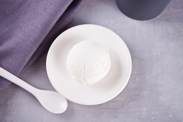 Gelato su un piatto in ceramica bianca con tovagliolo grigio e tazza grigia su un tavolo grigio