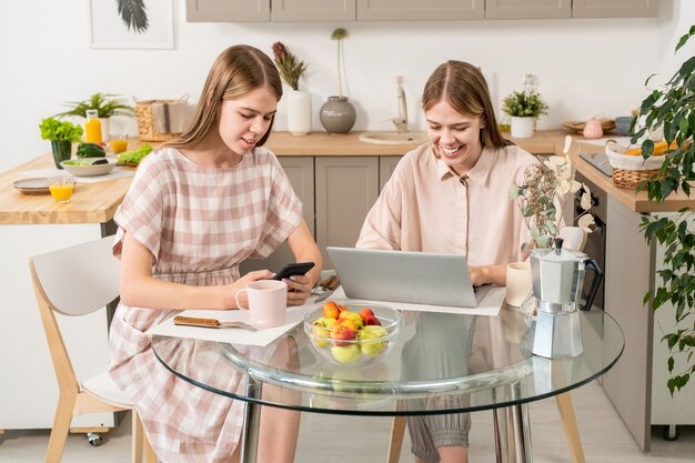 Gemelle contemporanee che usano gadget mobili sul tavolo della cucina