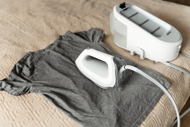 Generatore di vapore intelligente per stirare i vestiti con il concetto di lavoro domestico in modalità ecologica il ferro moderno è sul letto