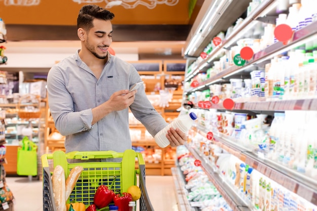 Generi alimentari maschi arabi che scansionano il latte tramite cellulare nel supermercato