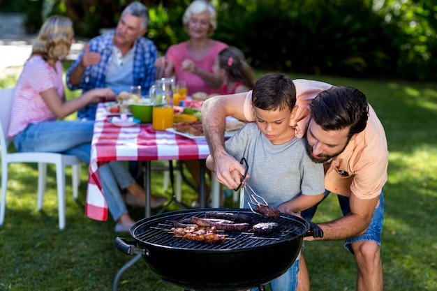 Generi il figlio d'istruzione che cucina sul barbecue con la famiglia