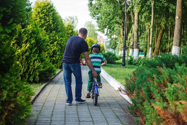 Generi il figlio di aiuto per guidare la bicicletta nel parco dell&#39;estate. Vista posteriore