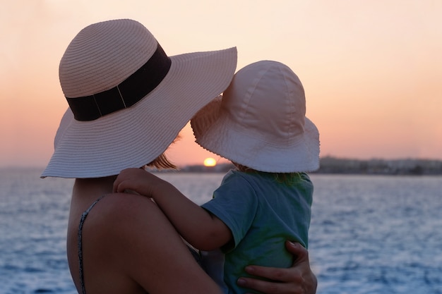Generi lo sguardo attraverso il mare sul tramonto mentre abbraccia il suo bambino