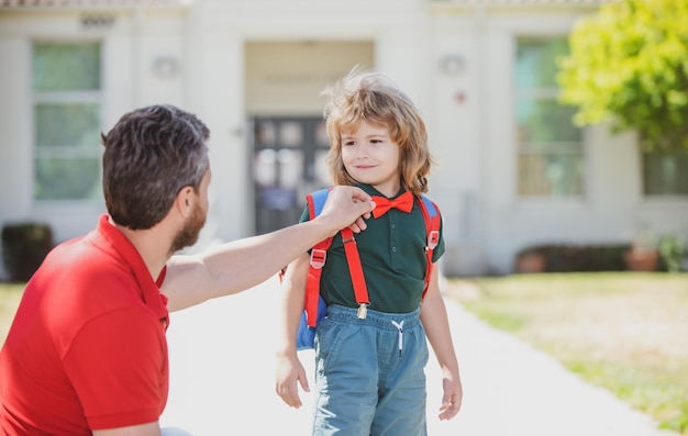 Genitore e allievo dell'insegnante di scuola primaria e scolaro carino con zaino vicino al parco scolastico