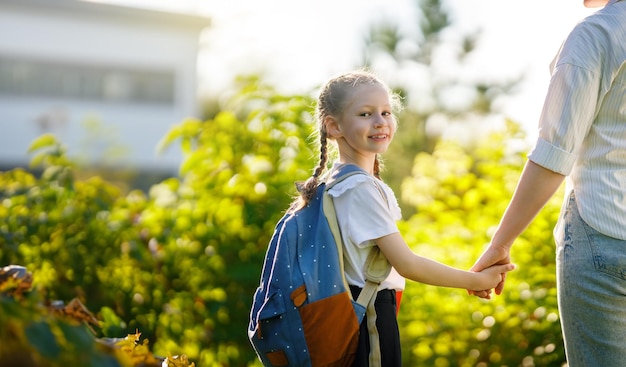 Genitore e allievo della scuola elementare che vanno mano nella mano Donna e ragazza con zaino