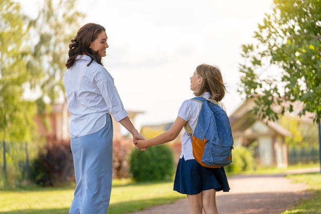 Genitore e allievo della scuola primaria vanno di pari passo. Donna e ragazza con zaino dietro la schiena. Inizio lezioni.