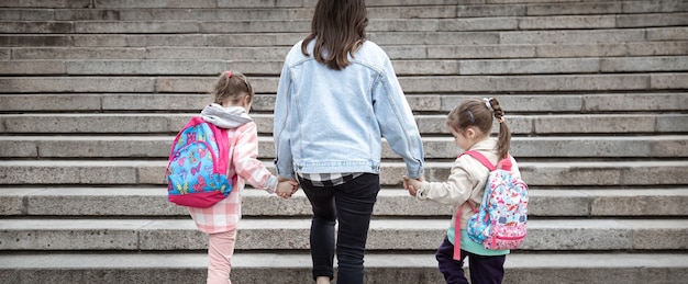 Genitore e allievo della scuola primaria vanno di pari passo. Mamma di due ragazze con uno zaino dietro la schiena. Inizio delle lezioni. Primo giorno d'autunno.