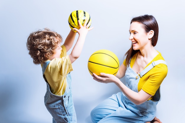 Genitore single giovane madre adulta che gioca con suo figlio con una palla da basket e da calcio. concetto gioca con i bambini. madre single. sport a scuola