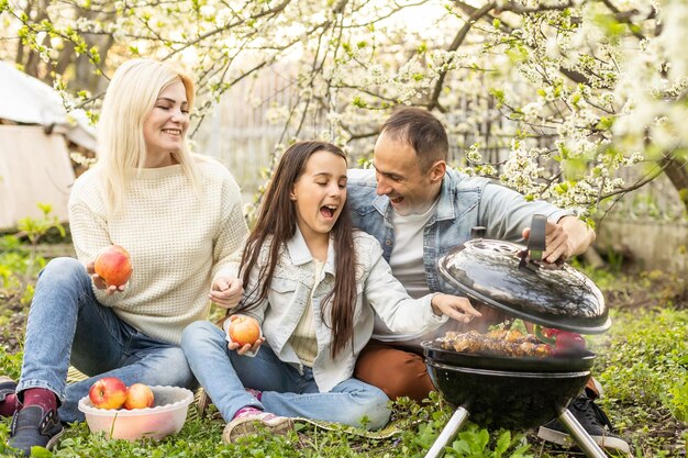 genitore sorridente che griglia carne con la figlia in campeggio.