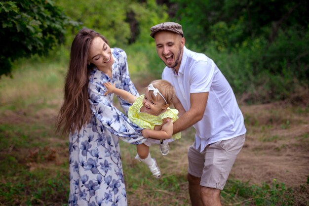 Genitori caucasici allegri giocano con la piccola figlia e ridono del giardino verde