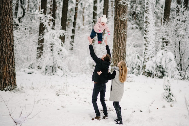 Genitori che giocano con sua figlia nel parco forestale invernale.