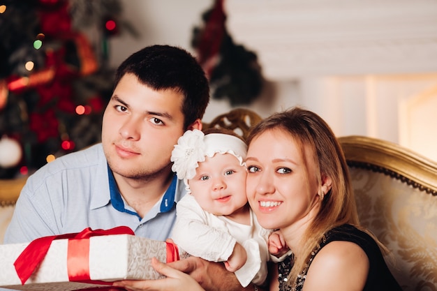 Genitori che si siedono sul pavimento con il bambino vicino all'albero di Natale.