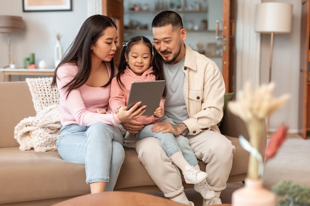 Genitori cinesi e bambino piccolo che usano il websurfing del tablet a casa