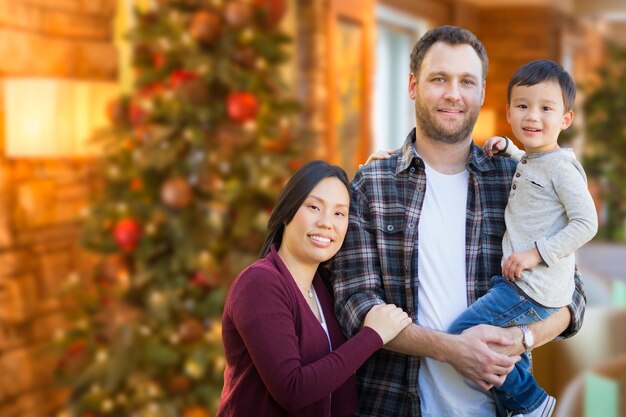 Genitori di razza mista cinesi e caucasici e figli all'interno davanti all'albero di Natale