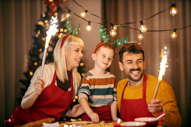 Genitori divertenti che tengono fuochi d'artificio e festeggiano Natale e Capodanno