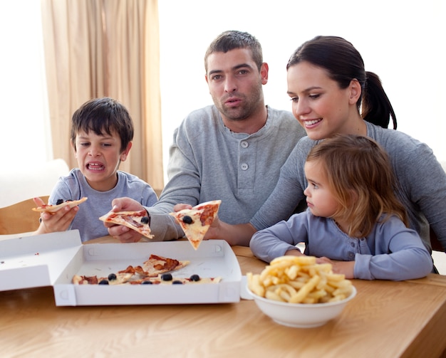 Genitori e bambini che mangiano pizza e patatine fritte su un divano