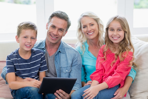 Genitori e bambini sorridenti che si siedono sul sofà con la compressa digitale in salone