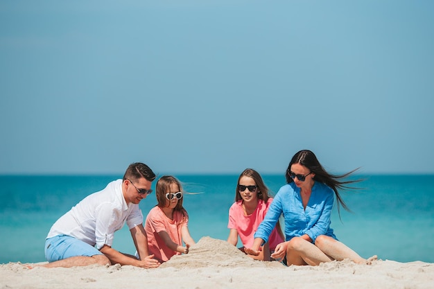 Genitori e due ragazze che giocano con la sabbia sulla spiaggia tropicale