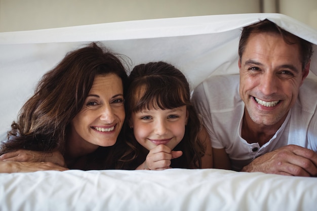 Genitori e figlia che sorridono sotto il lenzuolo