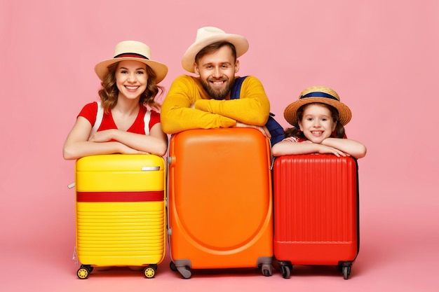 Genitori e figlia ottimisti che si appoggiano ai bagagli e sorridono per la macchina fotografica durante le vacanze estive su sfondo rosa