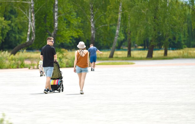 Genitori felici che camminano con il loro bambino nel passeggino al parco in una giornata di sole