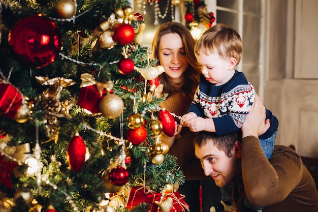 Genitori felici che mostrano la decorazione di natale sull'albero per il piccolo figlio.