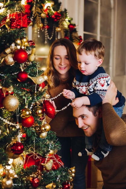 Genitori felici che mostrano la decorazione di natale sull'albero per il piccolo figlio.