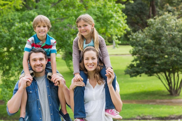 Genitori felici che trasportano i bambini sulle spalle al parco